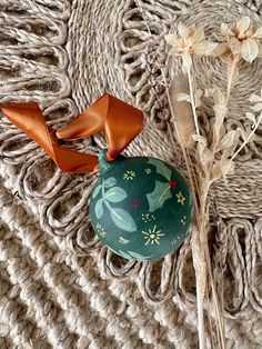 an ornament with a bow on it sitting next to some dried flowers and a piece of cloth