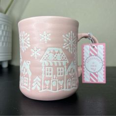 a pink coffee mug with white snowflakes on it and a tag attached to the handle