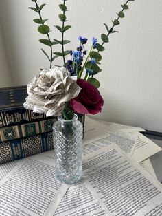 a vase filled with flowers sitting on top of an open book next to a stack of books