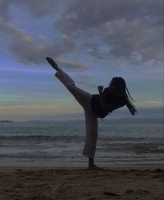 a woman doing a handstand on the beach in front of the ocean at sunset