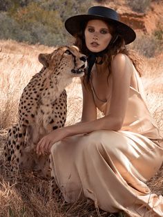 a woman in a dress and hat sitting next to a cheetah