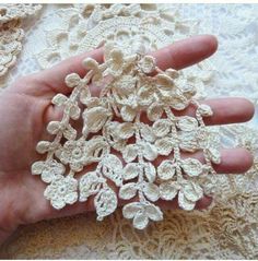 a hand is holding several crocheted flowers on a lace tablecloth, which looks like they have been made from yarn