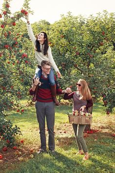 three people are standing in an apple orchard