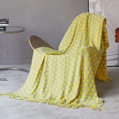 a yellow blanket sitting on top of a wooden chair next to a glass table and wall