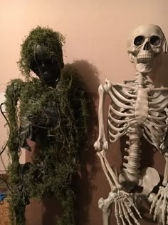 two skeletons are standing next to each other in front of a wall with moss growing on it