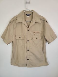 And then, this. Who knew? It's a Vintage 1980s (early!) Levi's for Men Tan Poly/Cotton Safari Photography Short Sleeve Shirt! Tag XL, Chest 46" Made in USA Classic safari shirt style in poly/cotton, made by Levi's in the USA. Style 70587-3123 Lovely vintage condition with no stains or holes we can see. Was it worn? And, again, what? I've never seen anything like this and it's utterly BOSS. Check that zip chest pocket. The metal buttons. Epaulets. Dig that collar.  Please see our other listings for more vintage Levi's garments with new items added nearly daily. PLEASE check the measurements as vintage clothing sizes may not comparable to contemporary sizes. Measurements: Label size: Extra Large Shoulder-to-shoulder: 19" Chest across: 23" Sleeve from shoulder: 11" Length in back from base of Safari Photography, Safari Shirt, Shirt Tag, Pocket Shirt, Vintage Textiles, Mens Oxfords, Baby Bear, Metal Buttons, Vintage Wool