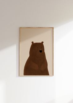 a brown bear sitting in front of a white wall with a wooden frame on it