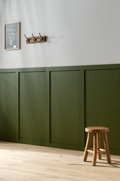 a wooden stool sitting on top of a hard wood floor next to a green wall