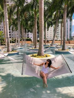 a woman laying in a hammock on the beach with palm trees around her