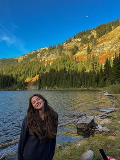 a woman standing next to a lake with mountains in the background