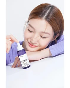 a woman is smiling and touching her face with a bottle of skin care product in front of her