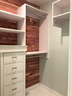 an empty closet with white drawers and wooden walls