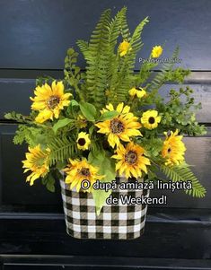 a black and white checkerboard vase with yellow sunflowers, ferns and greenery