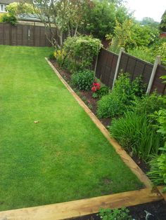 a garden with green grass and flowers in the back yard, next to a wooden fence