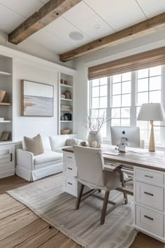 a home office with white furniture and wood beams on the ceiling, along with a large window