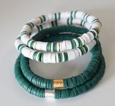 three green and white bracelets with gold accents on each one side, sitting on a white surface