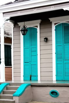 two blue shutters on the side of a gray house with steps leading up to it