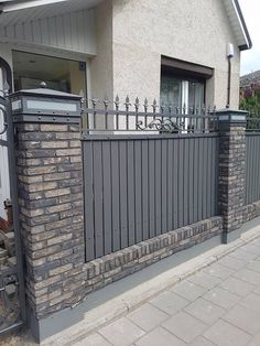 a house with a gate and brick wall next to the sidewalk in front of it