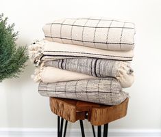 a stack of blankets sitting on top of a wooden stool next to a potted plant