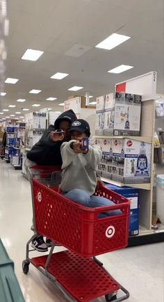 two people sitting in a shopping cart taking pictures with their cell phones at the store