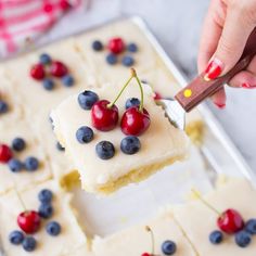 a person cutting into a cake with cherries and blueberries on it, while someone is holding a knife in the middle