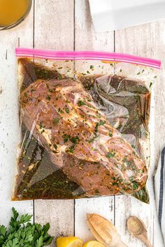 a bag filled with meat sitting on top of a table next to lemons and parsley