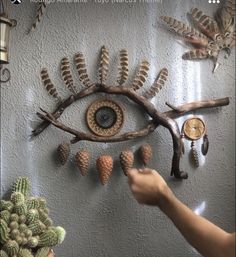 a person pointing at an eye made out of branches and pine cones on a wall