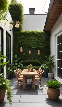 an outdoor dining area with potted plants on the wall and wooden table in front