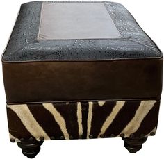 a zebra print ottoman sitting on top of a wooden stand with leather trimmings