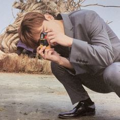 a man in a suit squatting down while holding a cell phone to his face