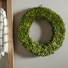 a green wreath hanging on the wall next to a coat rack with clothes in it