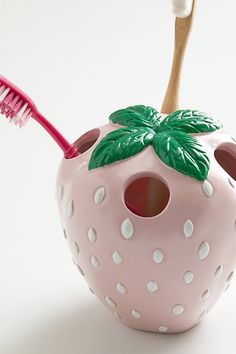 a pink strawberry shaped toothbrush holder with a green leaf on top and a white background