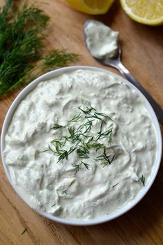 a bowl filled with white sauce and garnished with green herbs next to sliced lemons