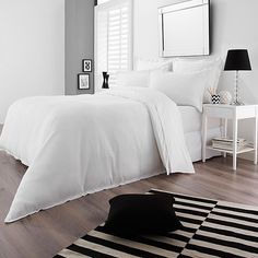 a bed with white sheets and pillows on top of a wooden floor next to a black and white rug