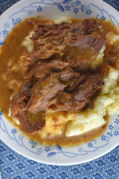 a blue and white plate topped with mashed potatoes and beef in gravy