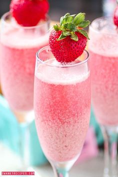 two glasses filled with pink liquid and topped with a strawberries on the rim,