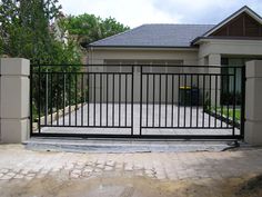 a gated driveway in front of a house with an iron fence and brick walkway