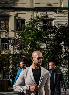 a man walking down the street with his hand on his hip wearing sunglasses and a gray jacket