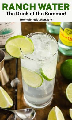 a glass filled with water and limes on top of a wooden table