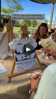 people sitting at an easel with flowers and paintings on the table in front of them