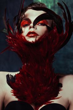 a woman with red makeup and feathers on her head is posing for a photo in front of a dark background