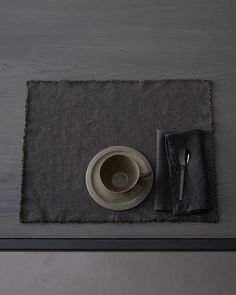 a place mat with a cup and saucer on it, next to a napkin