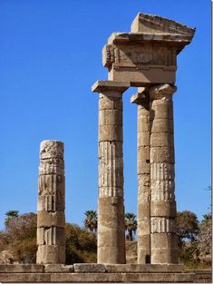 two large stone pillars sitting in the middle of a desert area with palm trees behind them