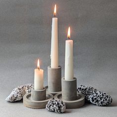 three candles sitting on top of each other with rocks around them in front of a gray background