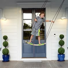 a young boy is swinging on a rope in front of a white house with blue doors