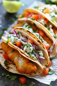 three fish tacos with salsa, onions and cilantro on paper wrappers