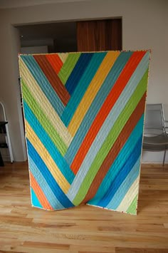 a multicolored quilt sitting on top of a hard wood floor next to a chair