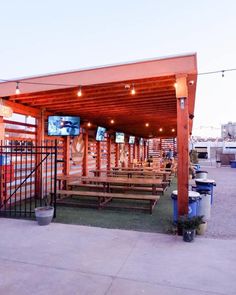 an outdoor seating area with wooden benches and televisions on the wall behind it at dusk