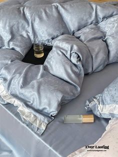 a bed with a blue comforter on top of it next to a bottle of perfume