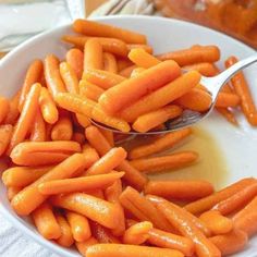 a spoon full of baby carrots sitting in a white bowl on top of a table